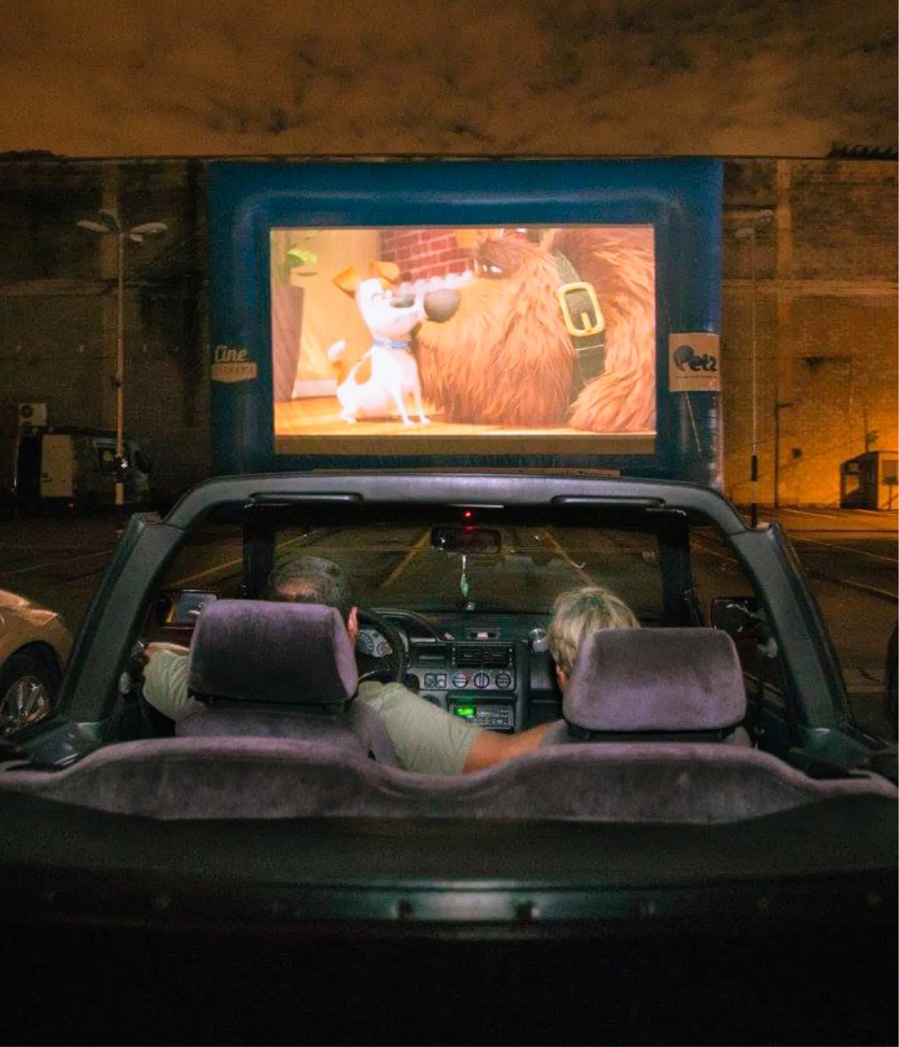 Casal num conversível assistindo a um filme na tela inflável do Cine Autorama
