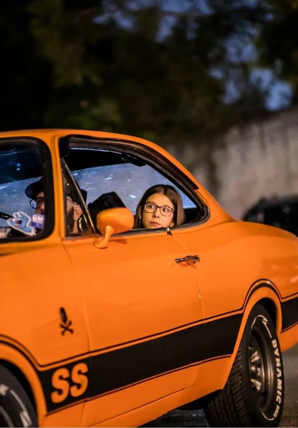 Menina olhando pela janela de um carro clássico laranja